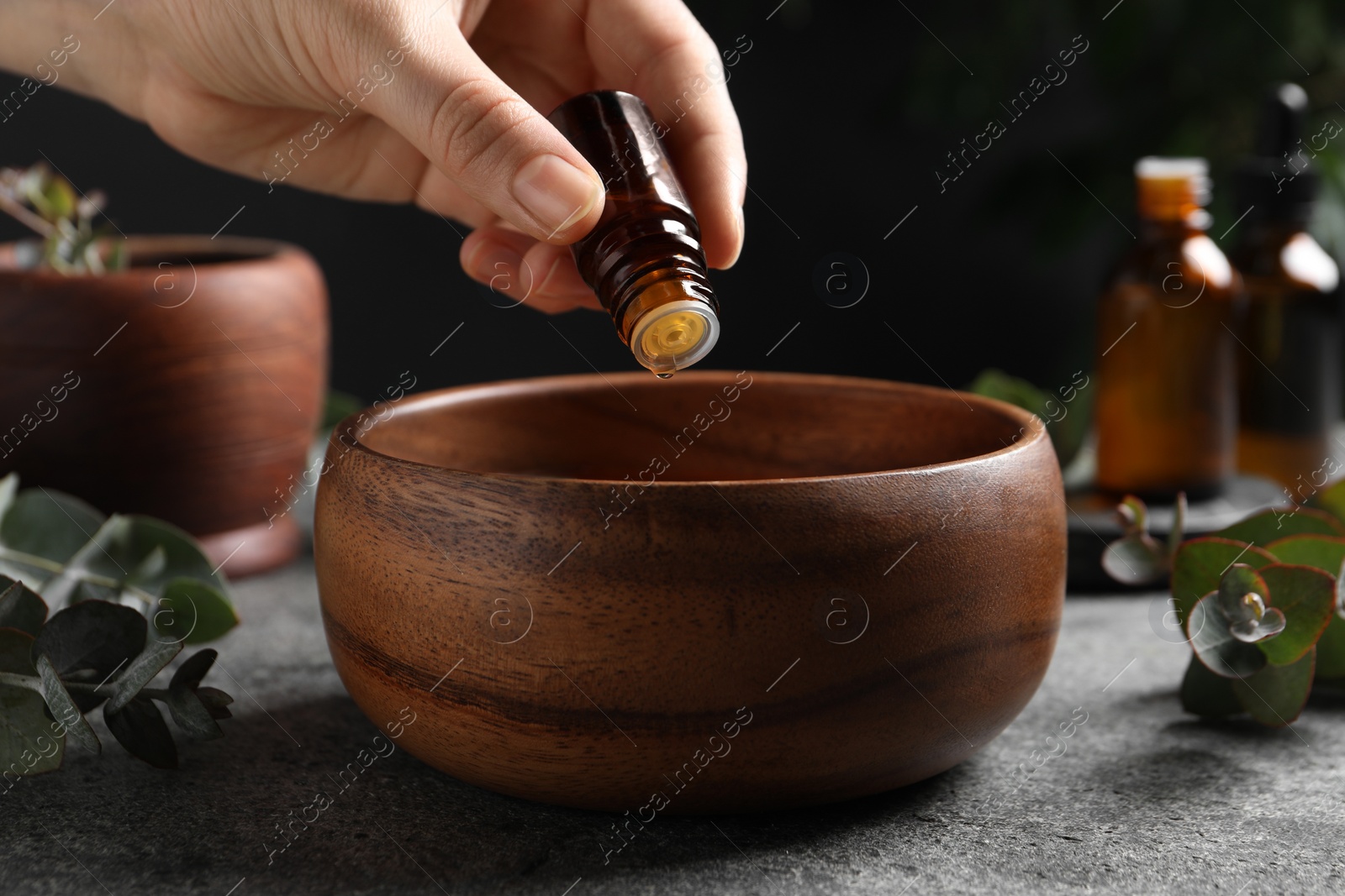 Photo of Woman dripping eucalyptus essential oil from bottle into bowl at light grey table, closeup