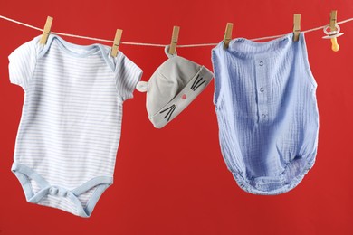 Photo of Baby clothes hanging on washing line against red background