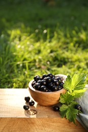 Ripe blackcurrants in bowl and leaves on wooden surface outdoors. Space for text