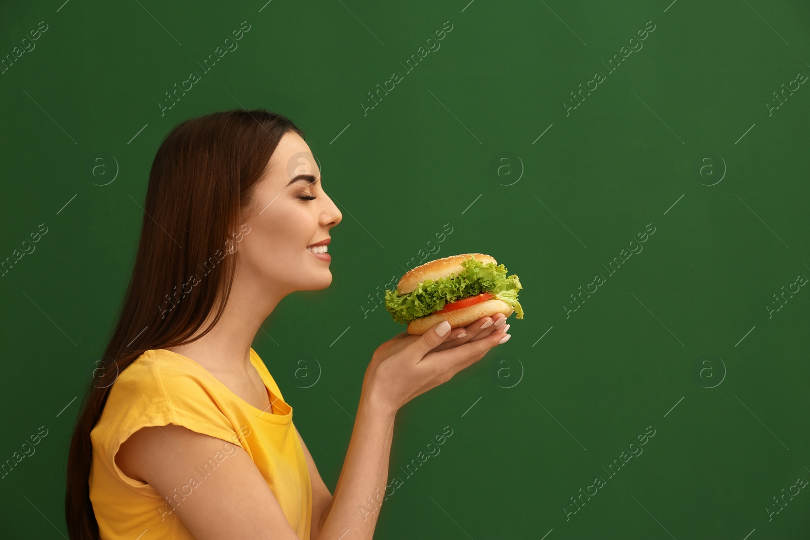 Photo of Young woman eating tasty burger on color background. Space for text