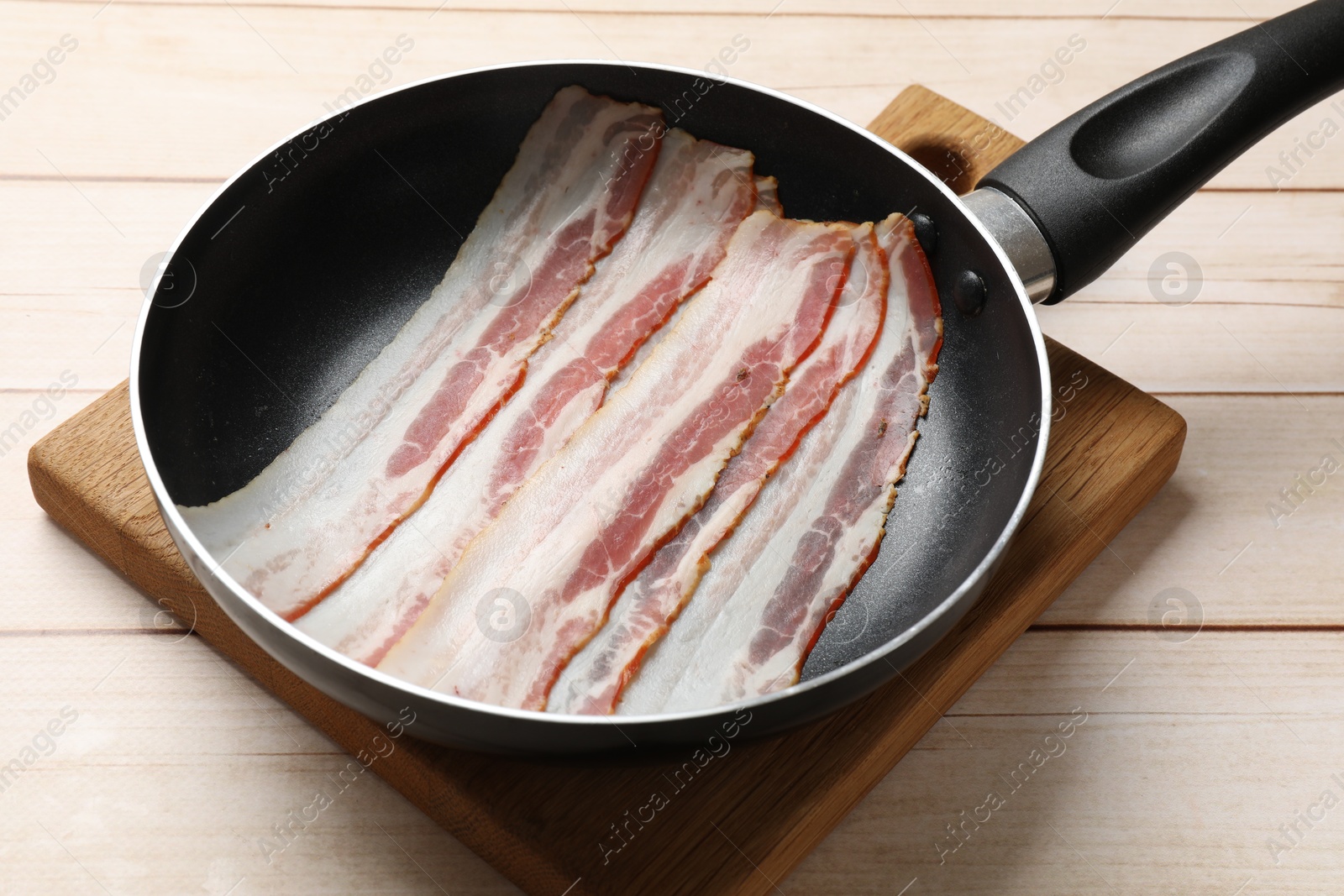 Photo of Slices of raw bacon in frying pan on wooden table, closeup