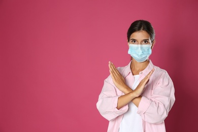 Photo of Woman in protective mask showing stop gesture on pink background, space for text. Prevent spreading of coronavirus