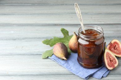 Photo of Jar of tasty sweet jam and fresh figs on grey table, space for text