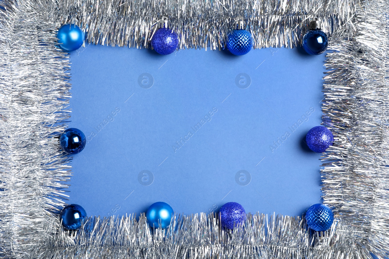 Photo of Frame of silver tinsel and Christmas balls on blue background, flat lay. Space for text