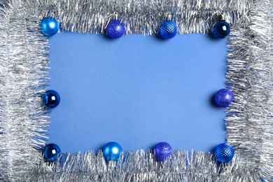 Photo of Frame of silver tinsel and Christmas balls on blue background, flat lay. Space for text