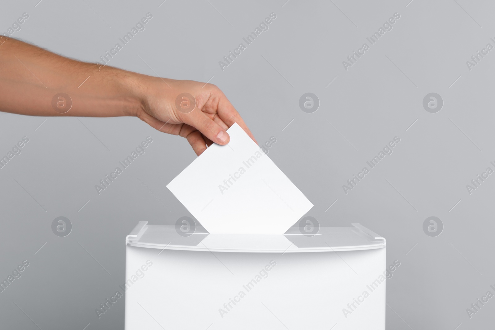 Photo of Man putting his vote into ballot box on light grey background, closeup