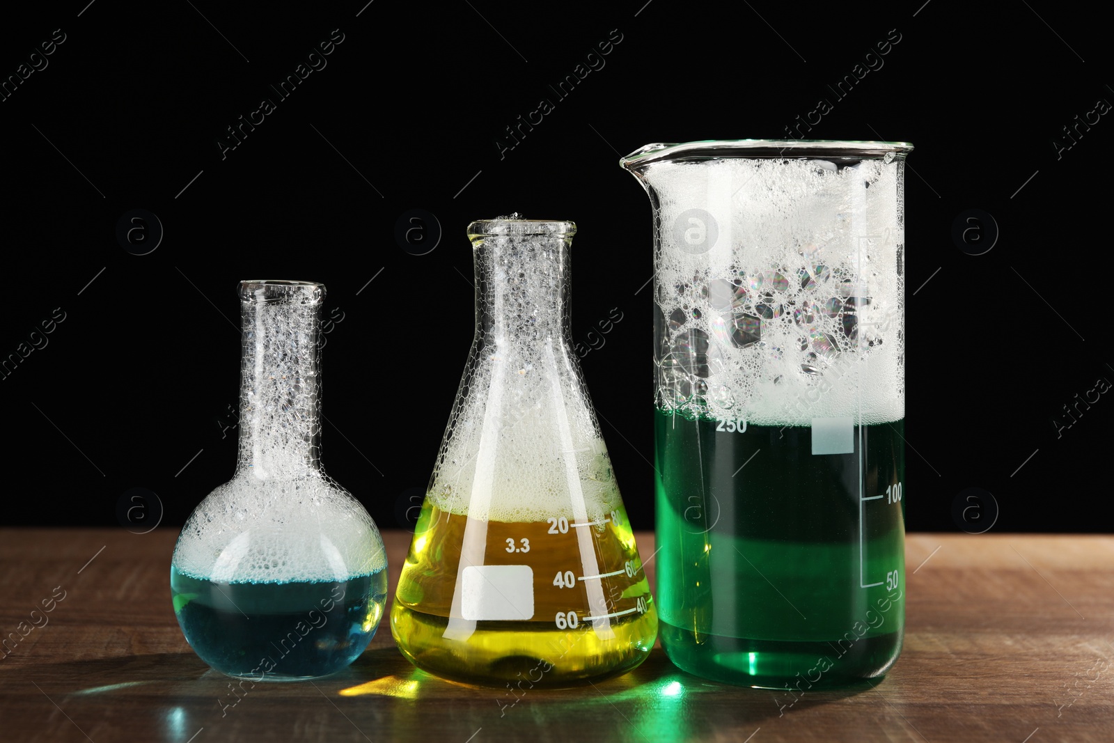 Photo of Laboratory glassware with colorful liquids on wooden table against black background. Chemical reaction