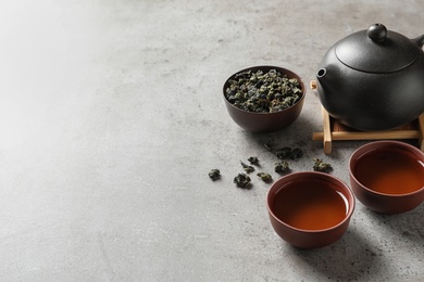 Teapot, cups of Tie Guan Yin oolong and tea leaves on table. Space for text