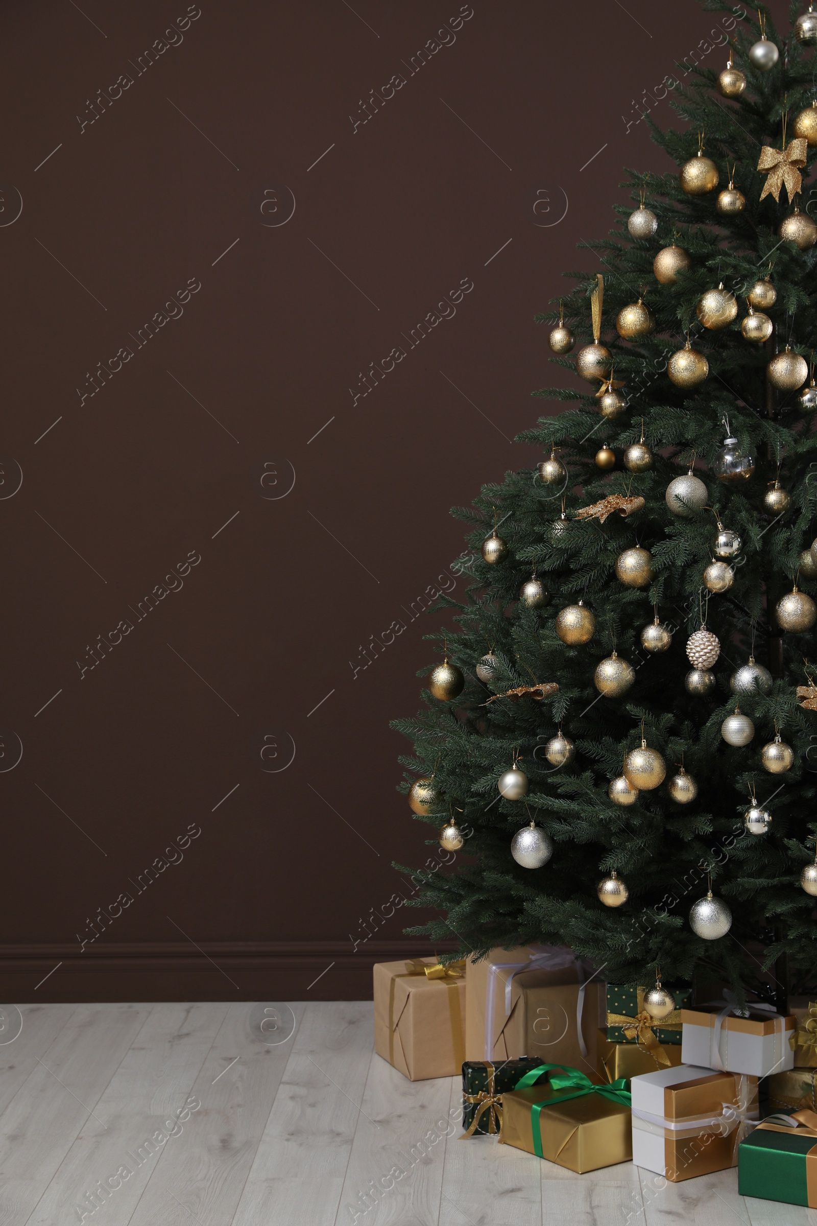 Photo of Beautifully decorated Christmas tree and many gift boxes near brown wall indoors, space for text