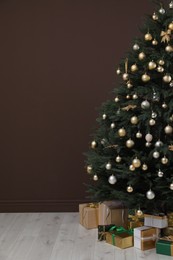 Beautifully decorated Christmas tree and many gift boxes near brown wall indoors, space for text