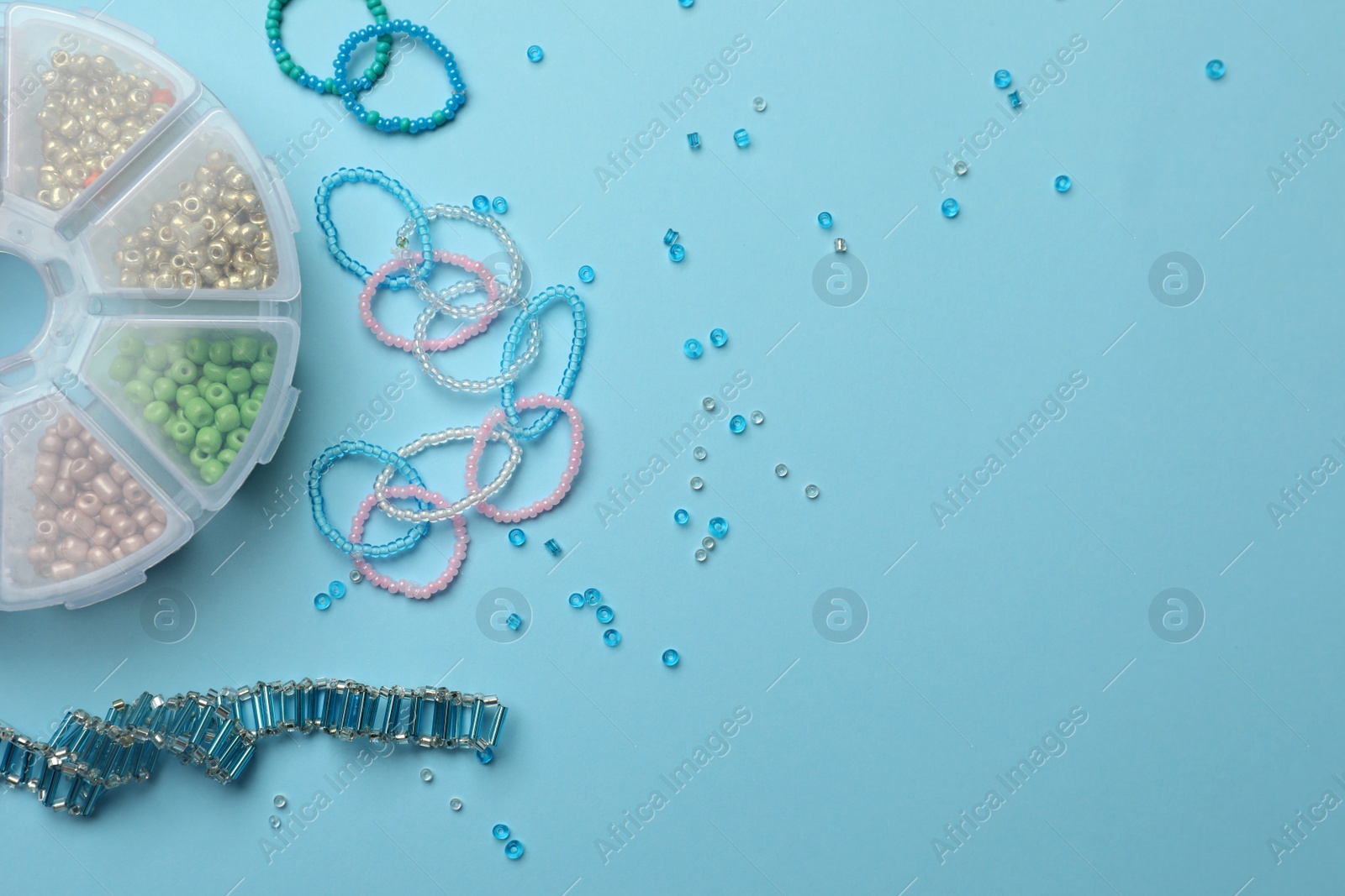 Photo of Beautiful handmade beaded jewelry and supplies on light blue background, flat lay. Space for text