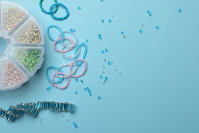 Photo of Beautiful handmade beaded jewelry and supplies on light blue background, flat lay. Space for text