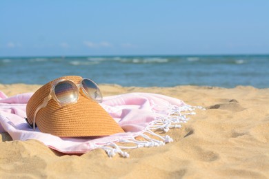Pink blanket with stylish visor cap and sunglasses on sandy beach near sea