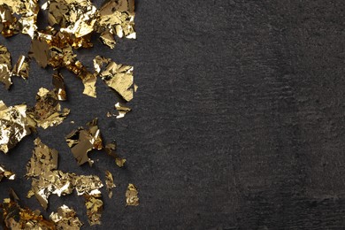 Photo of Many pieces of edible gold leaf on textured table, flat lay. Space for text