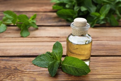 Photo of Bottle of essential oil and mint on wooden table, closeup
