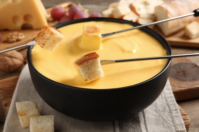 Photo of Dipping pieces of bread into tasty cheese fondue at table, closeup