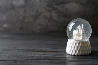 Snow globe with deer and trees on grey wooden table, space for text. Christmas season