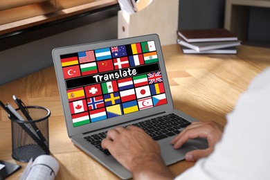 Translator using modern laptop with images of different flags on screen at table in office, closeup
