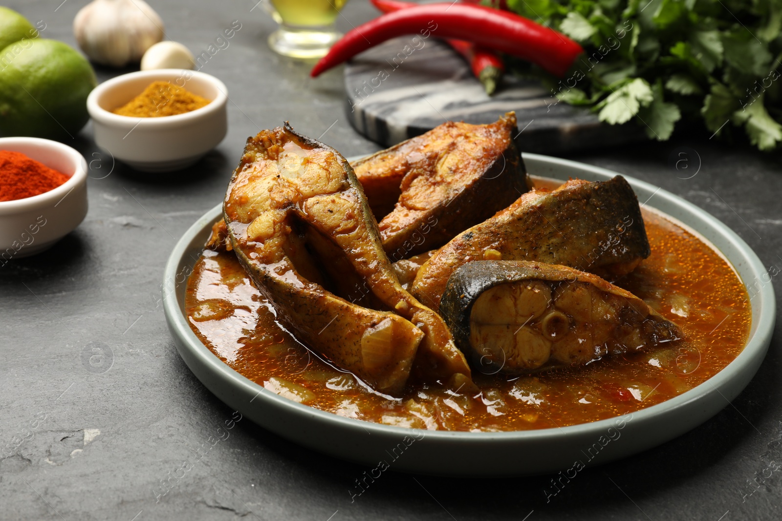 Photo of Tasty fish curry and ingredients on grey textured table, closeup. Indian cuisine