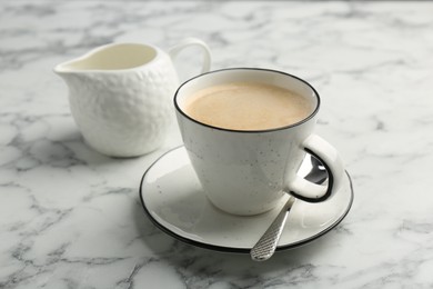 Photo of Tasty cappuccino in cup, spoon and saucer on white marble table, closeup