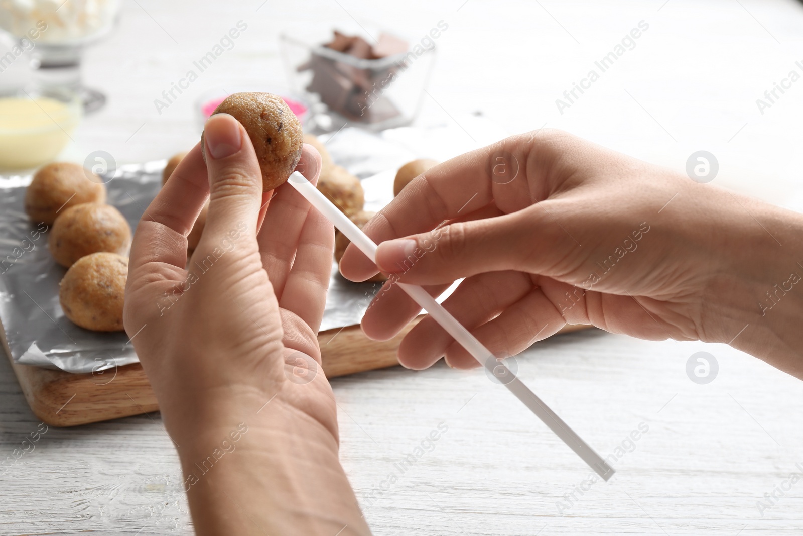 Photo of Woman making tasty cake pops at white wooden table, closeup