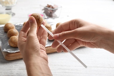 Photo of Woman making tasty cake pops at white wooden table, closeup