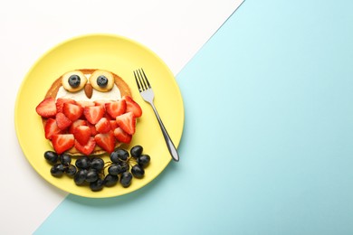 Photo of Creative serving for kids. Plate with cute owl made of pancakes, berries, cream, banana and almond on color background, top view. Space for text