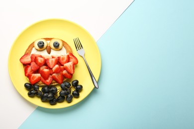 Creative serving for kids. Plate with cute owl made of pancakes, berries, cream, banana and almond on color background, top view. Space for text