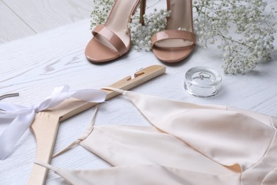 Photo of Beautiful wedding dress, shoes, engagement ring and flowers on white wooden background, closeup