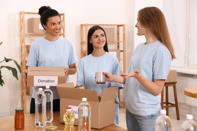 Group of volunteers packing food products at table in warehouse