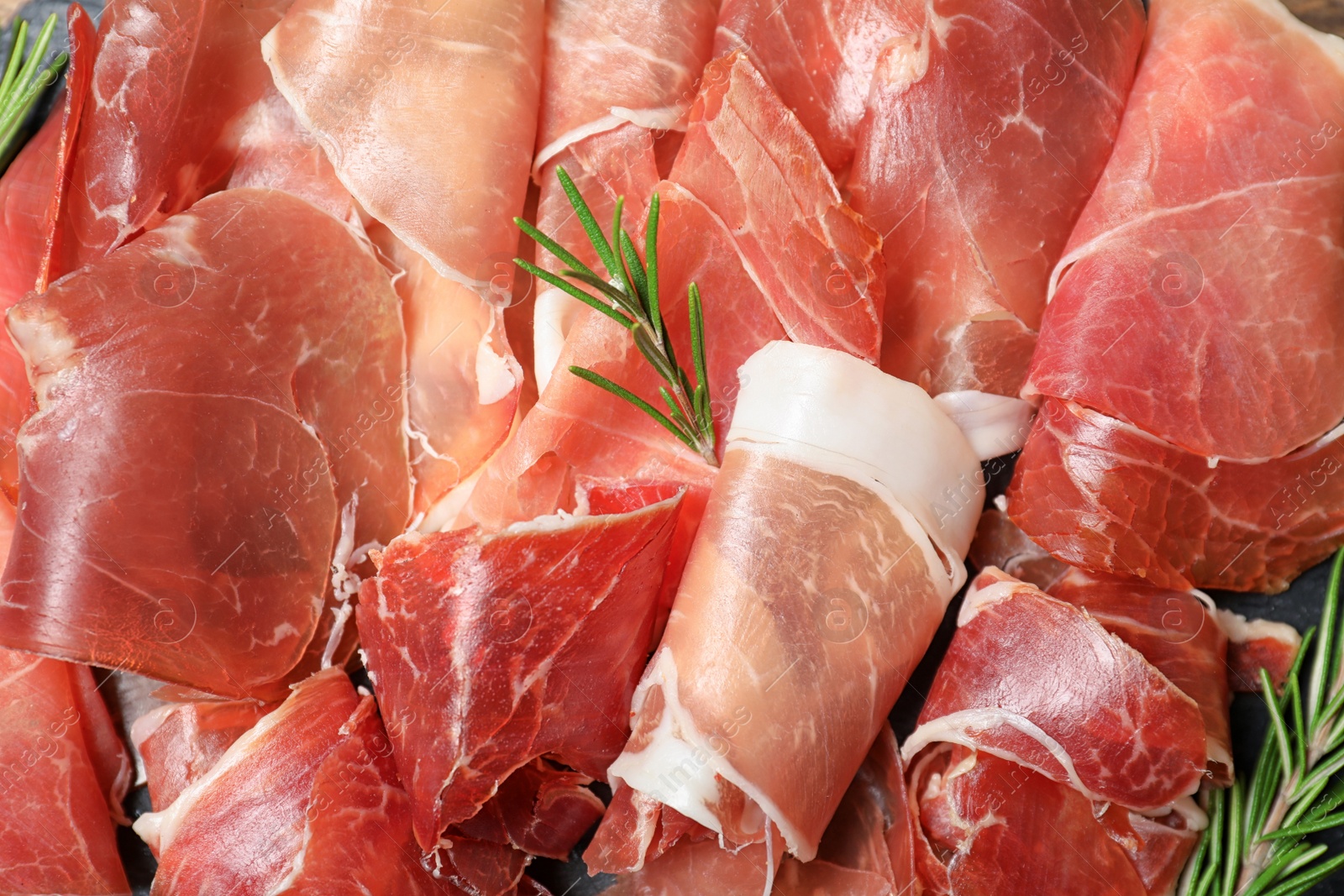 Photo of Tasty prosciutto with rosemary as background, top view