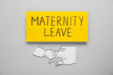 Photo of Note with words Maternity Leave and paper cutout of hands on light grey background, top view
