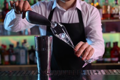 Photo of Alcoholic cocktail making. Bartender adding ice cubes into glass at counter in bar, closeup