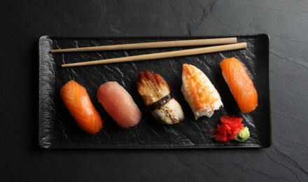 Serving board with delicious nigiri sushi, ginger and wasabi on black table, top view
