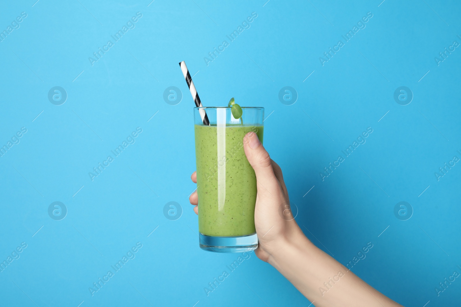 Photo of Woman holding glass of fresh green smoothie on light blue background, closeup