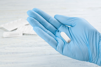 Woman holding suppository at white wooden table, closeup. Hemorrhoid treatment