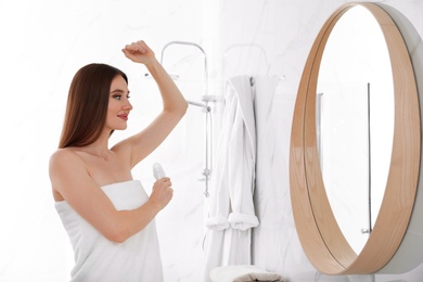 Photo of Beautiful young woman applying deodorant after shower in bathroom