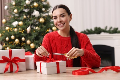 Photo of Happy woman decorating Christmas gift box at wooden table in room