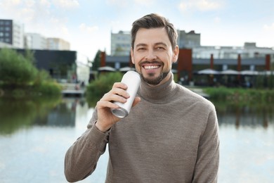 Happy man holding tin can with beverage near river outdoors