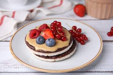 Photo of Crunchy rice cakes with peanut butter and sweet berries served on white wooden table, closeup