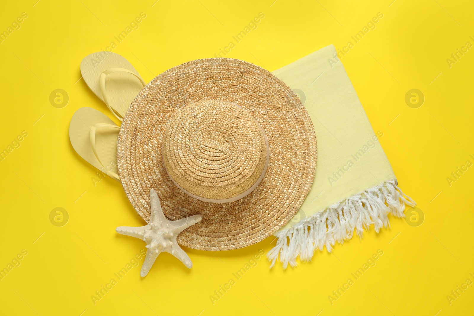 Photo of Beach towel, flip flops and straw hat on yellow background, flat lay