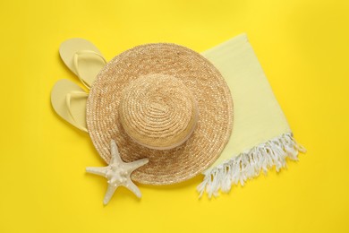 Photo of Beach towel, flip flops and straw hat on yellow background, flat lay