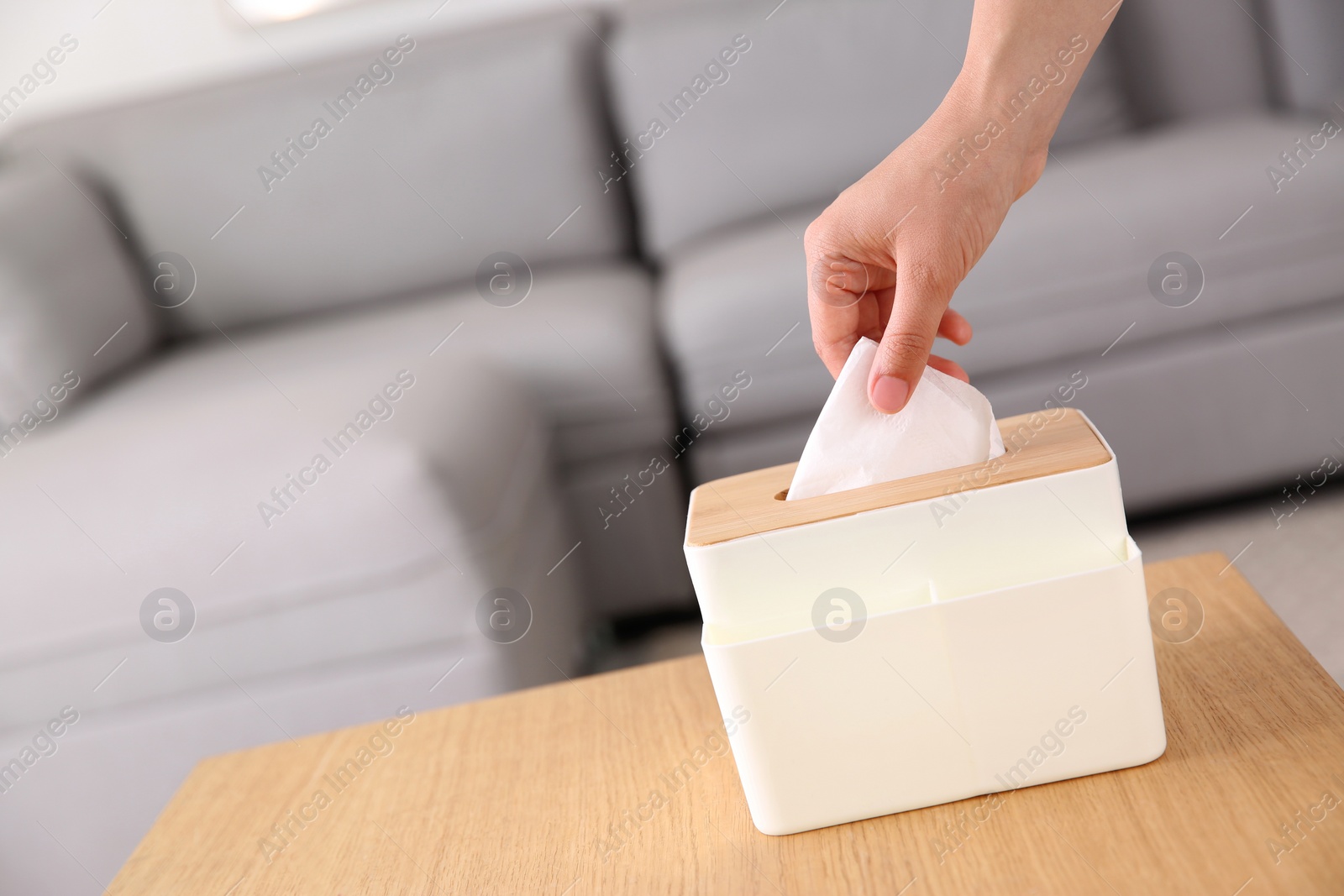 Photo of Woman taking paper tissue out of box on wooden table at home, closeup. Space for text