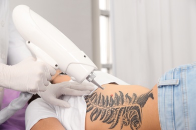 Photo of Young woman undergoing laser tattoo removal procedure in salon, closeup