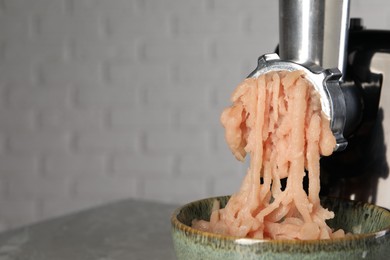 Photo of Electric meat grinder with chicken mince on table near light wall, closeup. Space for text