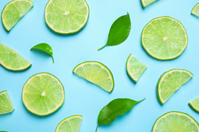 Juicy fresh lime slices and green leaves on light blue background, flat lay