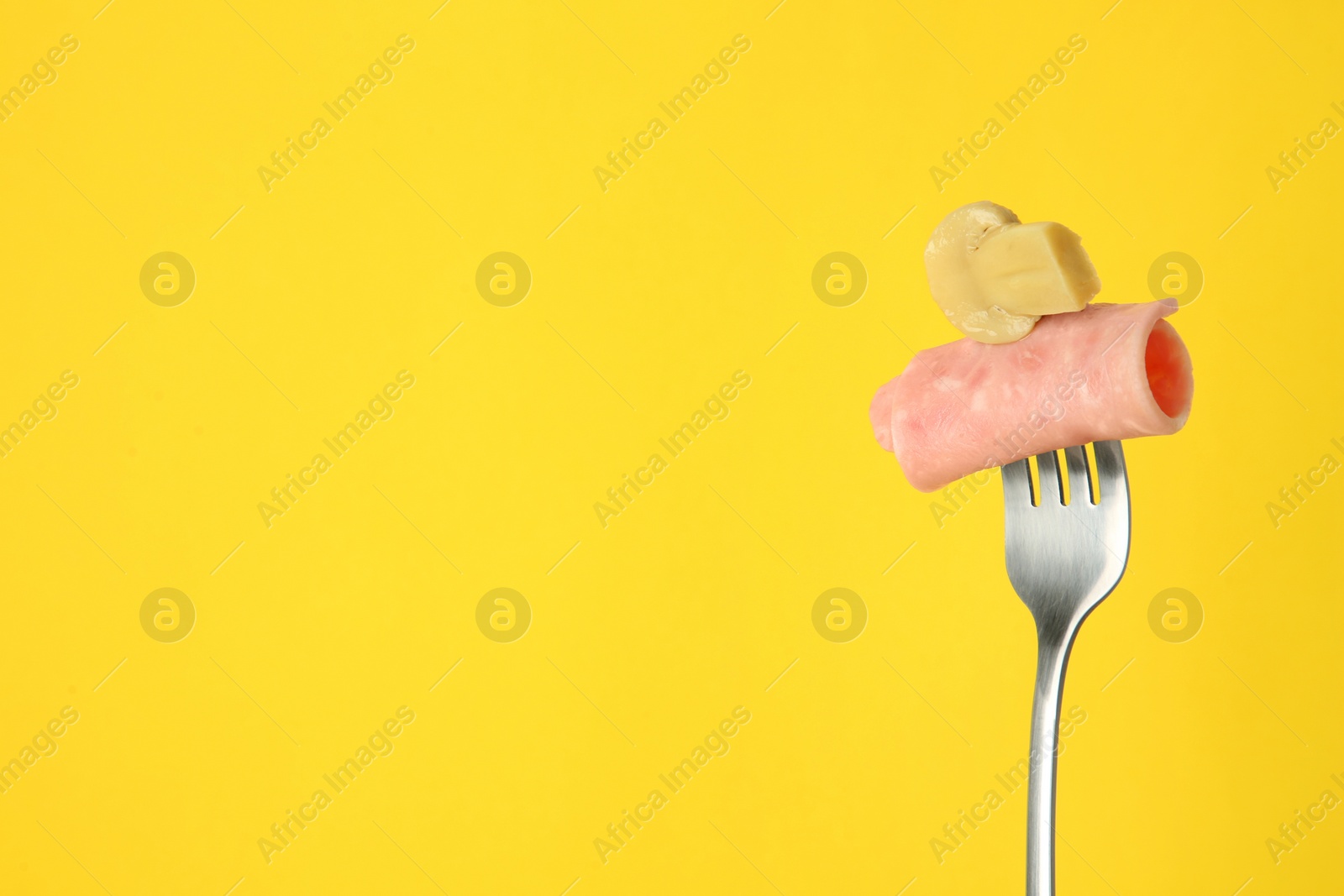 Photo of Fork with tasty slice of ham and pickled mushroom on yellow background, space for text