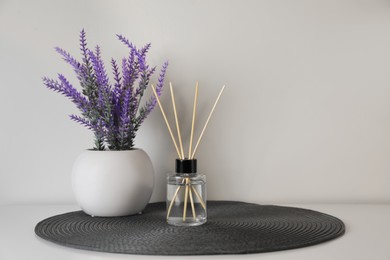 Photo of Aromatic reed air freshener and lavender flowers on white table. Space for text