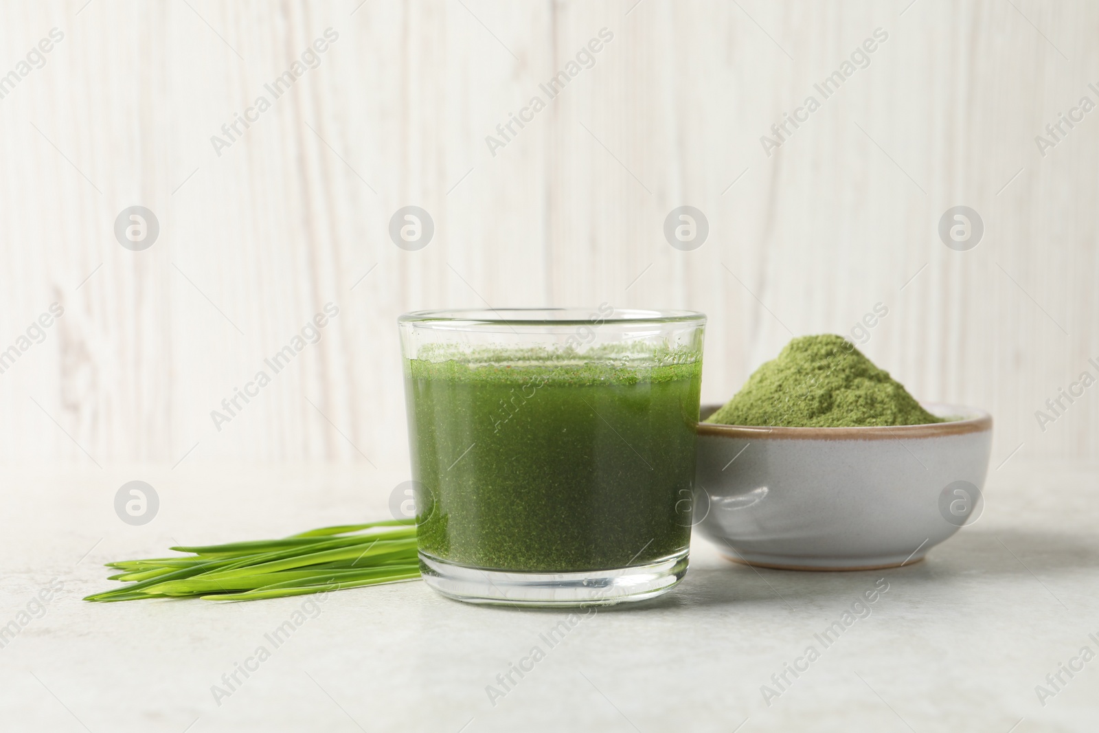 Photo of Wheat grass drink in glass, fresh sprouts and bowl of green powder on light table