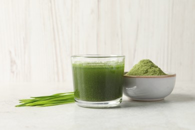 Photo of Wheat grass drink in glass, fresh sprouts and bowl of green powder on light table
